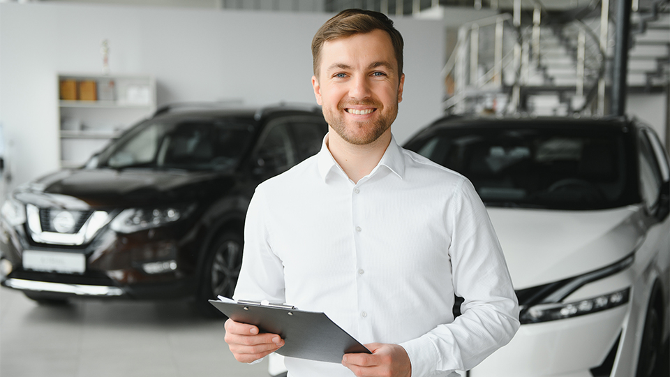 Porträt eines jungen Autoservice-Mitarbeiters in Hemd, der ein Klemmbrett hält und in die Kamera schaut.